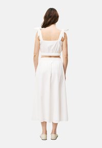 Witte katoenen tweedelige outfit bestaande uit een cropped top met strikbandjes en een bijpassende lange rok, getextureerd met subtiele patronen.