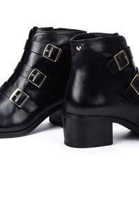 Botas de cuero negras hasta el tobillo con tres hebillas doradas, punta cuadrada y un tacón bajo tipo bloque. Acabado suave con una textura sutil.
