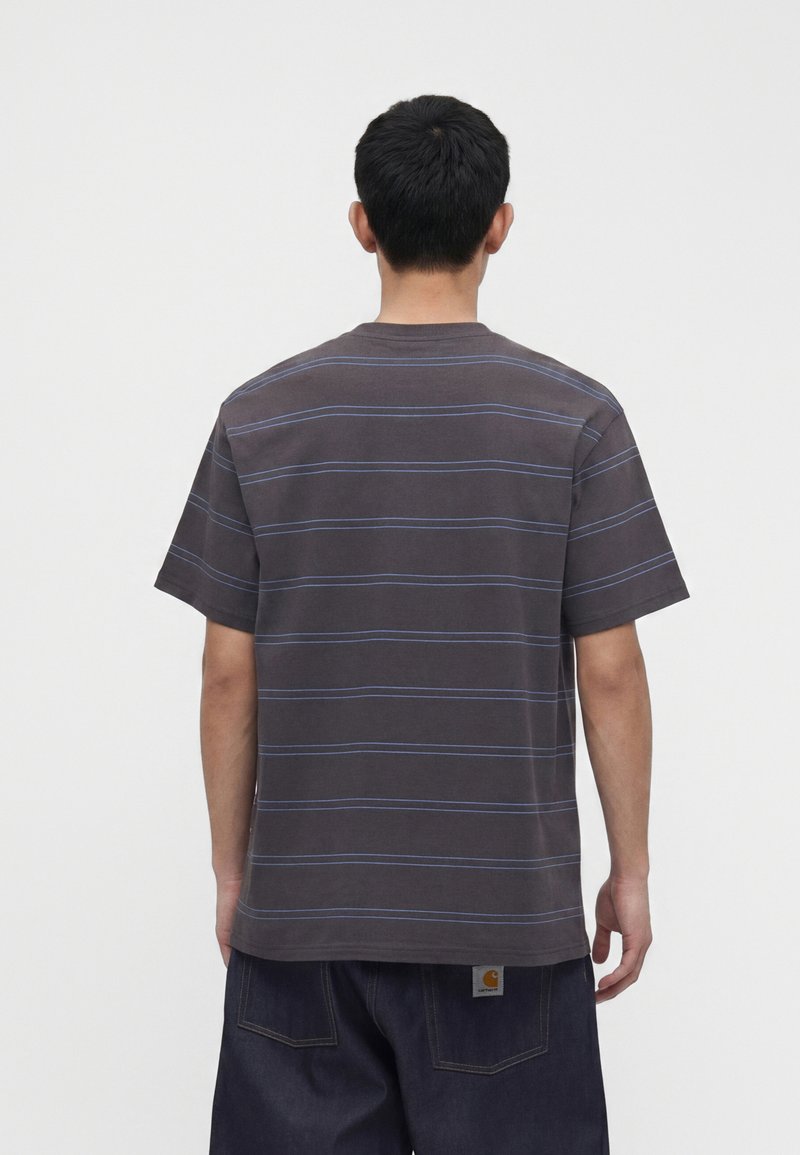 Uomo visto da dietro che indossa una maglietta grigio scuro a maniche corte con sottili strisce orizzontali blu e pantaloni di denim scuri con toppa di marca visibile.