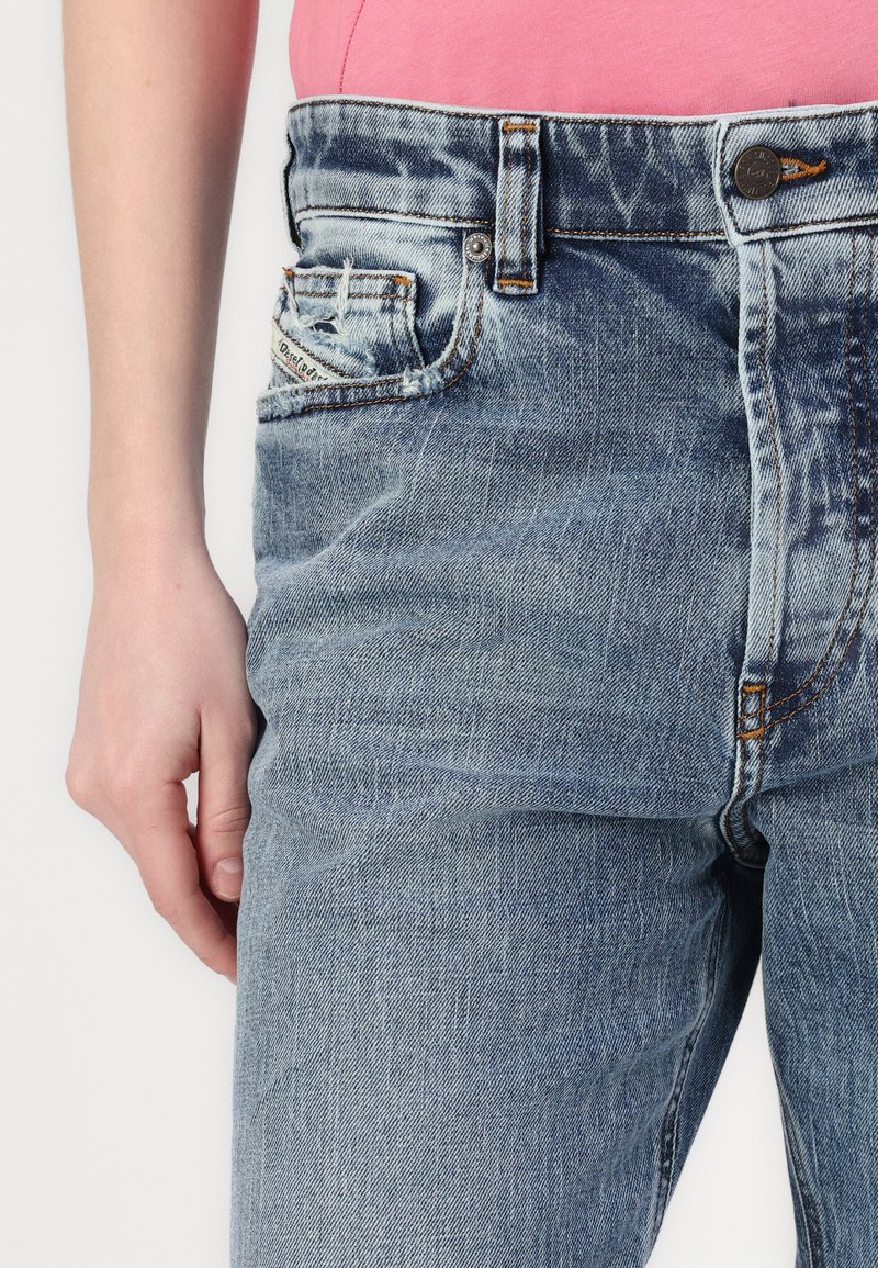 Hellblaue Denim-Jeans mit hoher Taille, verblasster Textur, Fünf-Taschen-Design und orangefarbener Nähtdetail nahe dem Taillenbund.