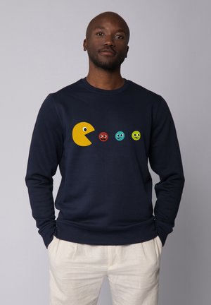 Navy Sweatshirt mit einem großen gelben Pac-Man-Graphic und vier bunten, runden Charakteren mit unterschiedlichen Gesichtsausdrücken.