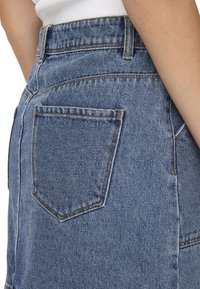 Gonna di jeans con un lavaggio blu sbiadito, dotata di tasca posteriore e cuciture ben visibili. Il tessuto ha una texture robusta e un aspetto solido.