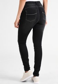 Vaqueros de mezclilla negros ajustados con cintura alta, con rayas blancas laterales, dos bolsillos traseros y una textura suave.