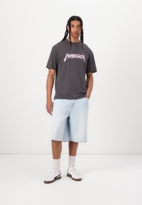 Hallitusest hall puuvillane T-särk roosa "Metallica" graafikuga, koos helesiniste denim lühikesed püksid. Valged tennisekenad pruuni aktsendiga ja sokid.