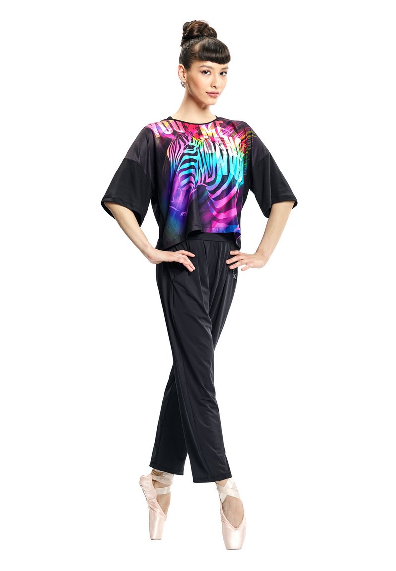 Top nero corto con stampa a zebre colorata; maniche ampie. Pantaloni neri con design affusolato, indossati con scarpe da balletto rosa chiaro.
