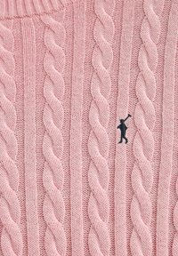 Rosa kabelstickat tyg med vertikala vridna mönster och en liten svart broderad figur som bär en golfklubba.