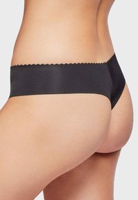 Zwarte naadloze slip met golvende rand, gladde textuur, minimale bedekking en een laag uitgesneden ontwerp, dat een slanke silhoeet benadrukt.