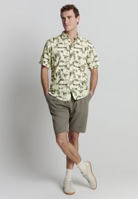 Korte mouwen overhemd met een roomkleurige basis en een groene abstracte print, gecombineerd met grijze shorts en lichte sneakers. Eenvoudig ontwerp.