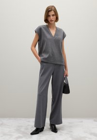 Grauer gestrickter Oberteil mit V-Ausschnitt und kurzärmligen Puffärmeln, kombiniert mit grauen weiten Hosen. Schwarze Ankle Boots und eine kleine schwarze Handtasche vervollständigen das Outfit.