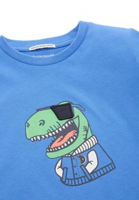 Modrá tričko vyrobené z organickej bavlny s kresleným dinosaurom v slnečných okuliaroch a džínsovou bundou. Mäkkučká štruktúra, ležérny dizajn.