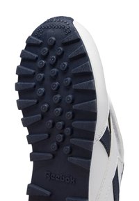 Zapatilla deportiva blanca con suela de goma de color azul marino oscuro. La suela presenta un patrón texturizado con puntos y crestas salientes para mayor tracción.