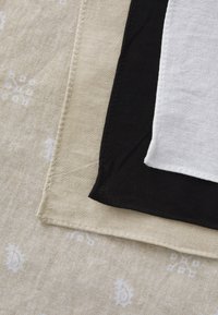 Three layered fabrics in beige, black, and white with contrasting textures. The beige fabric has subtle patterns, while the others are solid.