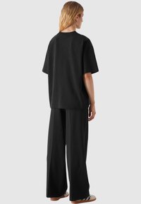 Fekete, oversized póló rövid ujjakkal, széles lábú fekete nadrággal párosítva. Simára szőtt anyag és minimalista dizájn.