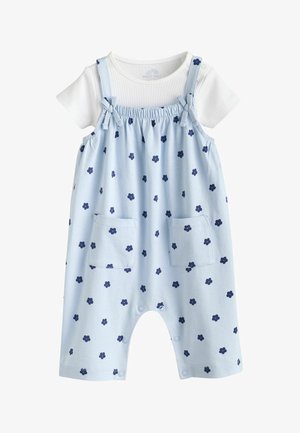 Blaues Overall-Kleid mit marineblauem Blumenmuster, elastischem Taillenbund, verstellbaren Schulterträgern und vorderen Taschen. Darunter ein weißes, geripptes T-Shirt.
