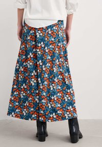 Maksimalus sijonas su mėlynu pagrindu, papuoštu oranžiniais, baltais ir žaliais gėlėmis. Pagamintas iš lengvos medžiagos, turi plazdančią struktūrą.