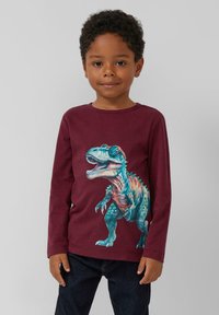 Bordeauxfarbenes langärmliges T-Shirt mit einem bunten Dinosaurier-Graphic, aus weichem Stoff, runder Ausschnitt und taillierter Passform. Kombiniert mit dunkelblauen Jeans.