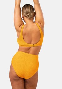 Gul texturerad bikiniuppsättning med en topp med rundad rygg och högmidjade bottnar, som visar ett konsekvent vågigt mönster.