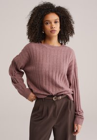 Gebreide trui met ribbels in gedempte mauve, met een ontspannen pasvorm en brede mouwen, gecombineerd met op maat gemaakte bruine broek en een dunne riem.