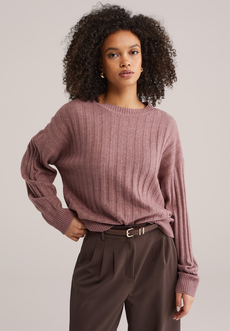 Gebreide trui met ribbels in gedempte mauve, met een ontspannen pasvorm en brede mouwen, gecombineerd met op maat gemaakte bruine broek en een dunne riem.