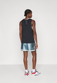 Svart ermeløs tank topp med V-formet utskjæring bak; metallisk teal shorts med hvit kant; hvite sportssokker; flerfargede joggesko.