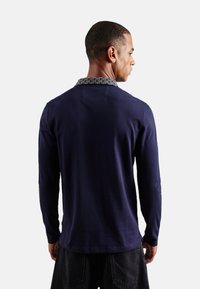 Camisa de manga larga azul marino con un cuello estampado, material de algodón y un corte relajado. Vista trasera, mostrando un diseño simple y hombros sin costuras.
