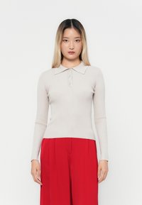 Beige ribbet langermet polo skjorte med krage og tre knapper, sammen med røde høyt liv bukser. Minimalistisk design, tettsittende fasong.