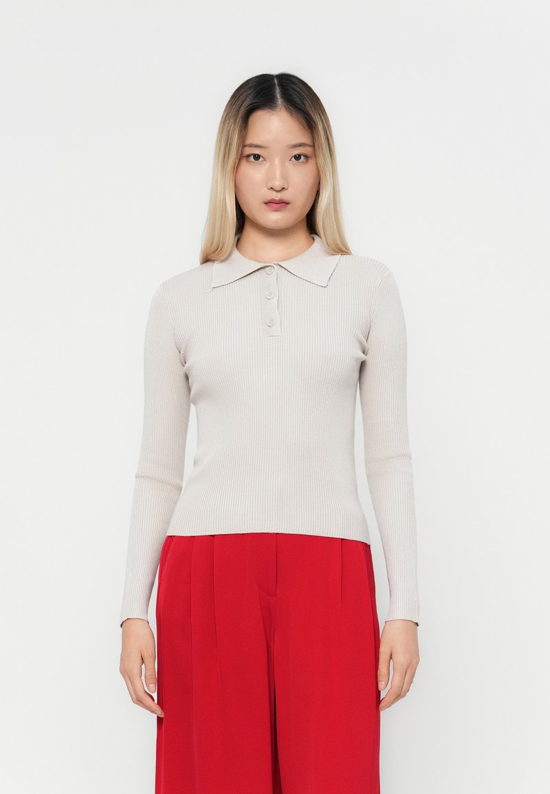 Beige ribbet langermet polo skjorte med krage og tre knapper, sammen med røde høyt liv bukser. Minimalistisk design, tettsittende fasong.