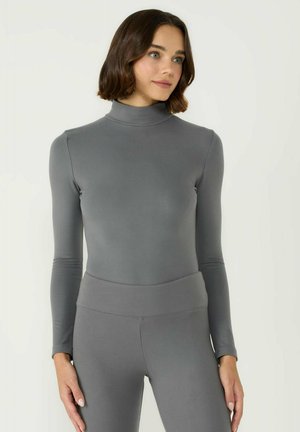 Grauer Langarm-Turtleneck aus glattem Material, mit einer figurschmeichelnden Silhouette und hohem Kragen, kombiniert mit passenden hoch geschnittenen Leggings.