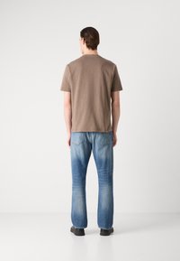 Brun kortermet t-skjorte kombinert med lyseblå straight-leg jeans. Jeansene har en lett falming og to baklommer med søm.