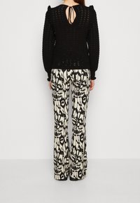 Pull noir texturé avec des manches bouffantes et un détail dos découpé, associé à un pantalon évasé à motifs noirs et blancs.