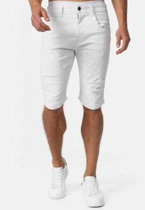 Pantalones cortos de mezclilla blanca con corte ajustado, que cuentan con bolsillos en ángulo, cierre de botón y un dobladillo limpio. Combinados con zapatillas blancas.