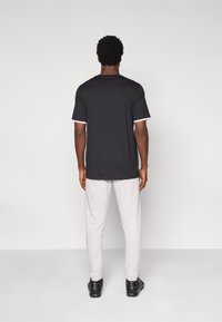 Camiseta negra de manga corta con detalles en blanco, combinada con pantalones gris claro. El material parece suave y ajustado en los hombros y la cintura.