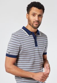 Camisa polo de manga corta con un patrón a rayas en tonos azul y crema, con un cuello azul oscuro y puños de canalé. Tejido de mezcla de algodón.