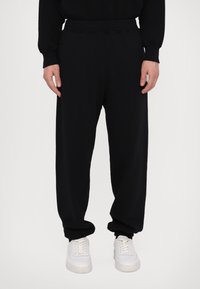 Schwarze Jogginghosen mit einer lockeren Passform, ausgestattet mit einem elastischen Bund, Bündchen an den Knöcheln und einer glatten Textur, kombiniert mit weißen Turnschuhen.