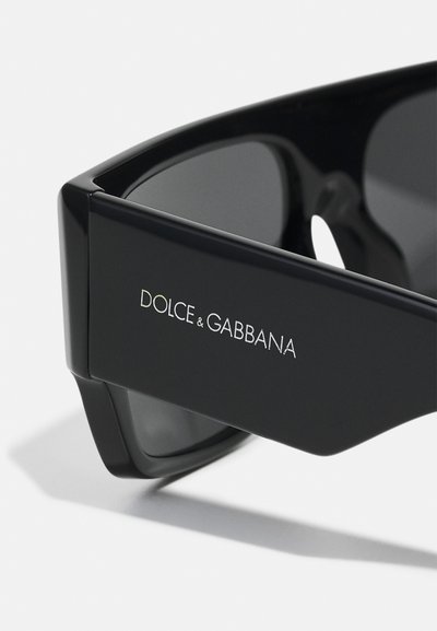 Ochelari de soare negri cu un finisaj lucios, având numele mărcii „DOLCE & GABBANA” embosat pe lateral. Designul unghiular subliniază estetica modernă.