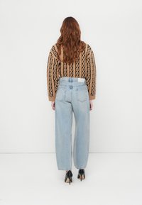 Brunmønstret strikket genser, lyseblå vide jeans, svarte høyhælte sko; bakfra som viser genser og denim detaljer.