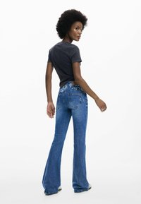 Lahendatud sinised teksad, millel on lillemustriga tikandid tagumistel taskutel, kombineeritud istuva süsihalliga t-särgiga. Sile teksatekstuur ja vabam istuvus.