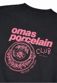 Čierna mikina s ružovým grafickým textom: "omas porcelain CLUB" a ilustráciou šálky na čaj s kvetinovými detailmi a nápisom "MAY CAUSE FOOD COMA."