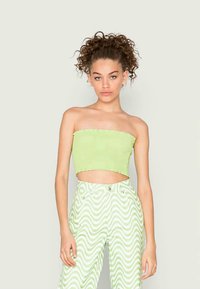 Top cropped sem alças de cor verde-claro com nervuras e uma bainha bruta, combinado com calças de cintura alta apresentando um padrão ondulado em branco e verde.