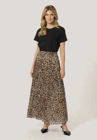 Plissé maxi-skjorte i beige med leopardmønster, parret med en sort t-shirt med korte ærmer og sorte hælede sko.