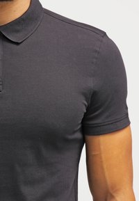 Polo à manches courtes en coton gris foncé, avec un col classique, des coutures visibles et une texture lisse et homogène.