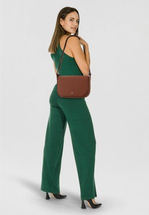 Borsa a tracolla in pelle marrone con finitura testurizzata, dotata di chiusura a patta e tracolla regolabile, indossata sopra una tuta verde.