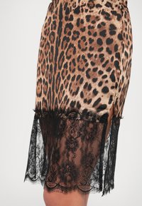 Φούστα με λεοπάρ σχέδιο σε μπεζ και μαύρο σατέν με διάφανο μαύρο δαντελένιο τελείωμα. Διαθέτει πλευρικές σχισμές με διακόσμηση από δαντέλα στο κάτω μέρος.