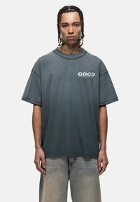 Grijs oversized t-shirt van zachte stof, met korte mouwen en een ronde halslijn. Opmerkelijke grafische tekst aan de voorkant in het wit en groen.