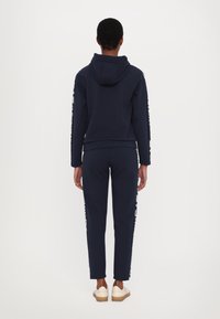 Conjunto de sudadera con capucha y pantalones jogger en azul marino, hecho de material suave. Presenta una capucha, un ajuste slim y detalles de marca en blanco en las mangas y los laterales.
