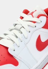 Λευκά και κόκκινα αθλητικά παπούτσια Nike με λευκές κορδόνες, κόκκινη σήμανση Nike και κόκκινο λογότυπο Jumpman στη γλώσσα.