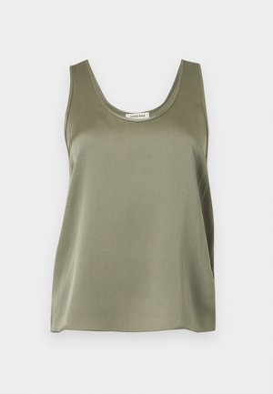 Femme mince à la peau foncée debout, portant un haut sans manches en satin vert olive et une jupe assortie fendue, et des ballerines beiges pointues.