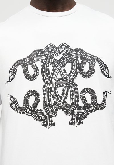 Λευκό πουκάμισο με συμμετρικό μαύρο γραφικό που απεικονίζει τέσσερα διαπλεκόμενα φίδια με μοτίβα διαμαντιού και καρό.