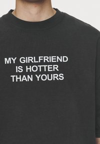 Black sweatshirt with a classic crew neck. Features bold white text saying "MY GIRLFRIEND IS HOTTER THAN YOURS" across the front.