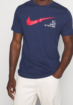 T-shirt in cotone blu navy con un grande logo rosso del swoosh Nike e il testo "NIKE SWOOSH ON TOUR 2020" in bianco sul davanti.